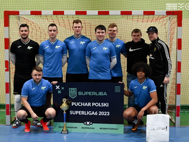 Na zdjęciu zwycięska druzyna turnieju Futsal Białobrzegi, piłkarze pozują na tle bramki z pucharem i z kartą superligi szódtek - zdobyta nagrodą