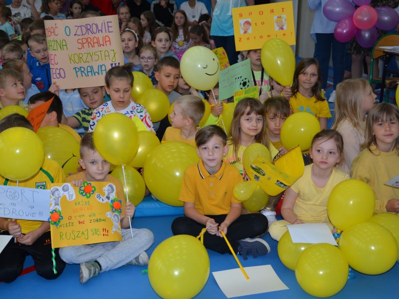 Na zdjęciu uczniowie ze SP nr 3 podczas Dnia Dziecka. Uczniowie z żółtymi balonami i transparentami promującymiu zdrowie