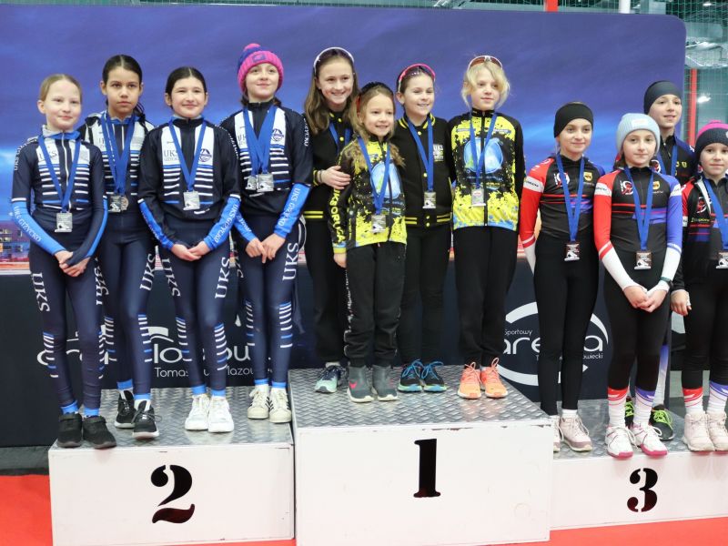 Na zdjęciu młodzi panczeniści na podium. Zdjęcie grupowe, panczeniści z medalami i w strojach sportowych