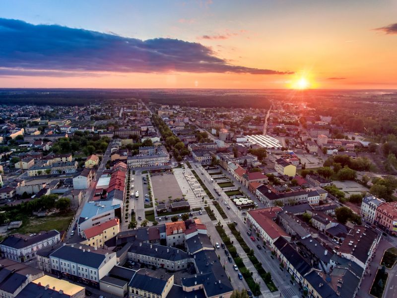 Panorama centrum Tomaszowa z lotu ptaka. Nad dachami domów wschodzi słońce