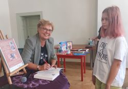 Na zdjęciu pisarka, autorka ksiązek dla dzieci z młodsa czytelniczką. Autorka składa autograf na swojej książce